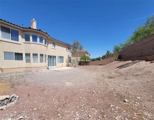 rear view of house featuring fence, stucco siding, and a chimney