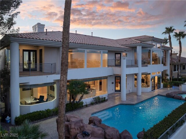 5020 Spanish Heights Dr, Las Vegas, NV 89148 - back of house at dusk with a balcony, a tile roof, a patio area, stucco siding, and a pool with connected hot tub