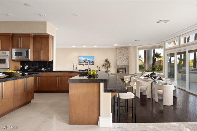 5020 Spanish Heights Dr, Las Vegas, NV 89148 - kitchen with stainless steel microwave, a sink, a kitchen breakfast bar, brown cabinets, and recessed lighting
