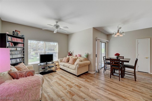 living area with a wealth of natural light, light wood-style flooring, and ceiling fan with notable chandelier