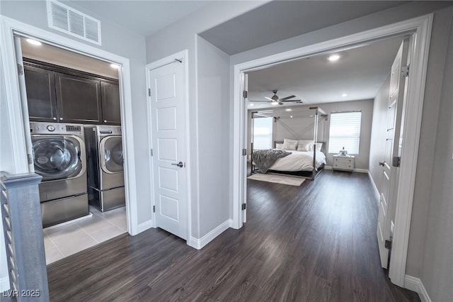 washroom with dark wood-type flooring, visible vents, washing machine and dryer, baseboards, and cabinet space
