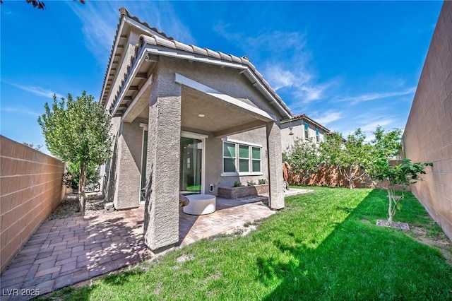 back of property featuring a yard, a fenced backyard, a tile roof, a patio, and stucco siding