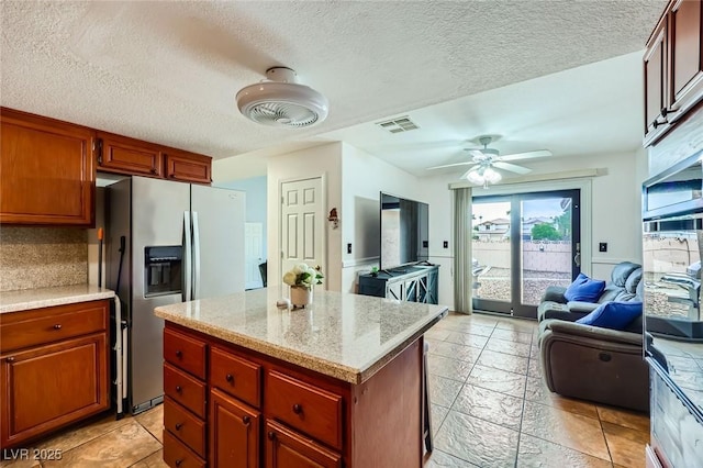 kitchen with visible vents, a center island, stainless steel refrigerator with ice dispenser, open floor plan, and ceiling fan