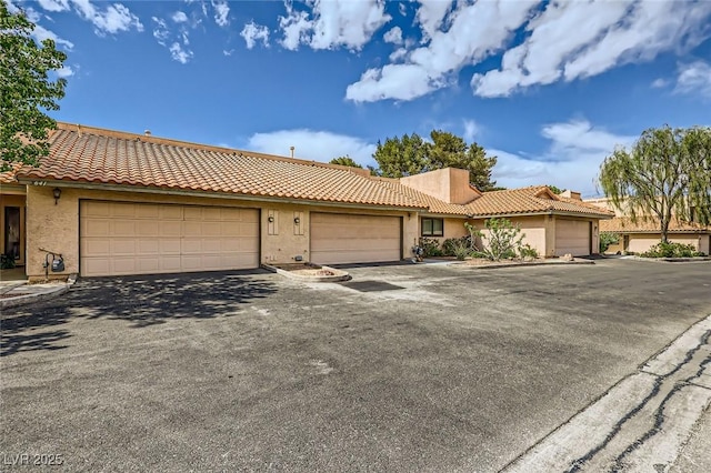 ranch-style home with an attached garage, a tile roof, aphalt driveway, and stucco siding