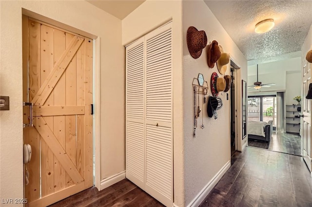 hall featuring dark wood-type flooring, a textured ceiling, and baseboards