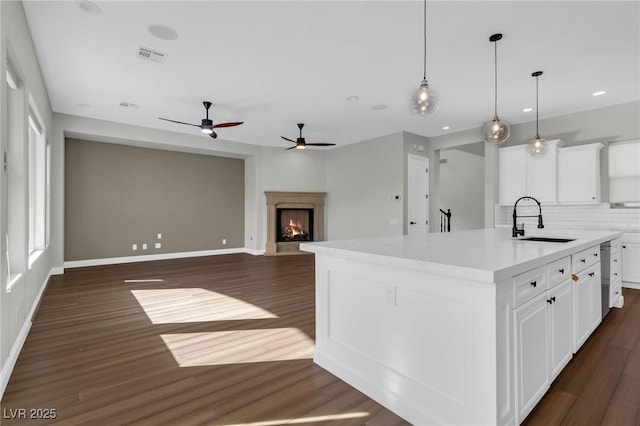 2805 Proust Ct, Henderson, NV 89044 - kitchen featuring tasteful backsplash, a kitchen island with sink, dark wood-style floors, a lit fireplace, and light countertops