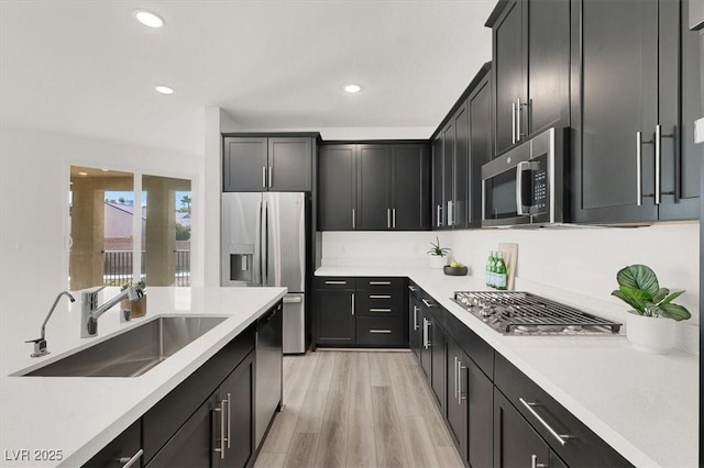 kitchen featuring a sink, dark cabinetry, stainless steel appliances, light countertops, and recessed lighting
