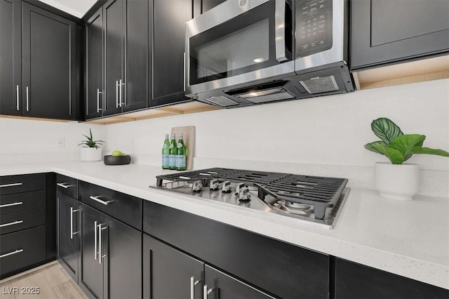 kitchen featuring dark cabinetry, light wood-type flooring, appliances with stainless steel finishes, and light countertops