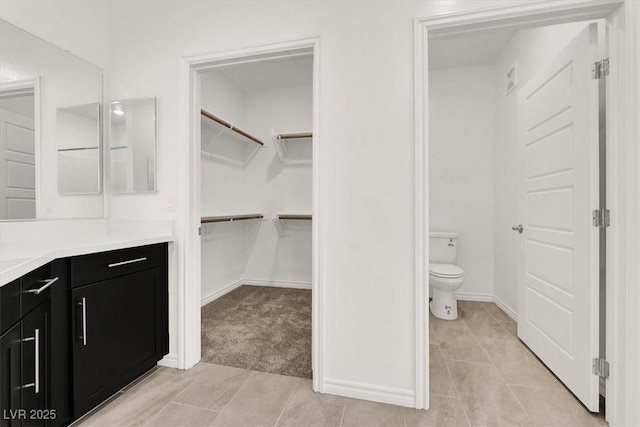bathroom with a spacious closet, vanity, tile patterned flooring, and toilet
