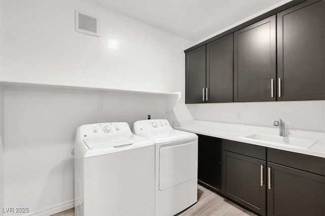 clothes washing area with a sink, washer and dryer, cabinet space, light wood finished floors, and visible vents