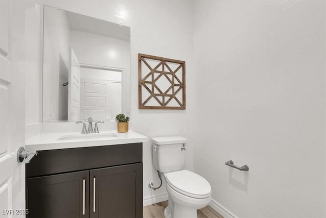 half bathroom with toilet, vanity, wood finished floors, and baseboards