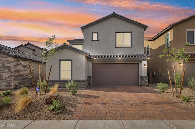 traditional-style home with stucco siding, decorative driveway, stone siding, a tile roof, and a garage