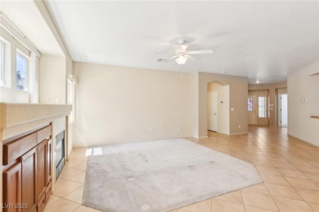 3029 Paseo Hills Way, Henderson, NV 89052 - unfurnished living room featuring light tile patterned floors, a ceiling fan, a tiled fireplace, and arched walkways