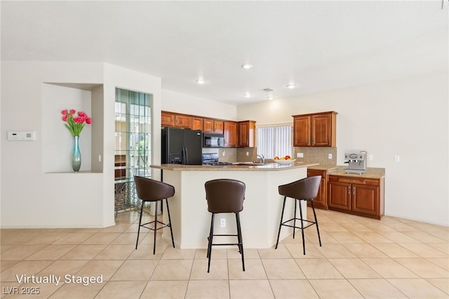 3029 Paseo Hills Way, Henderson, NV 89052 - kitchen with black appliances, a breakfast bar, brown cabinetry, a kitchen island with sink, and a sink