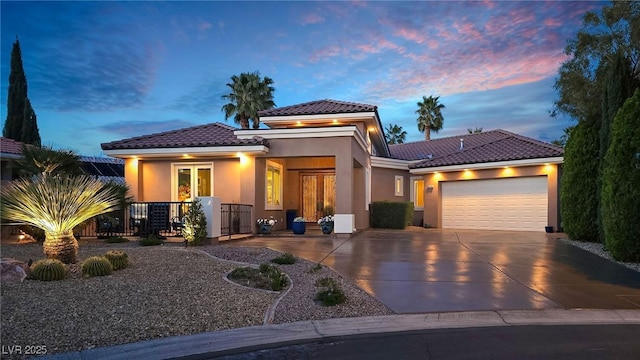 prairie-style house featuring a tile roof, stucco siding, french doors, an attached garage, and driveway
