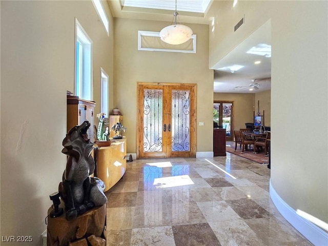 foyer with french doors, a towering ceiling, baseboards, crown molding, and a ceiling fan