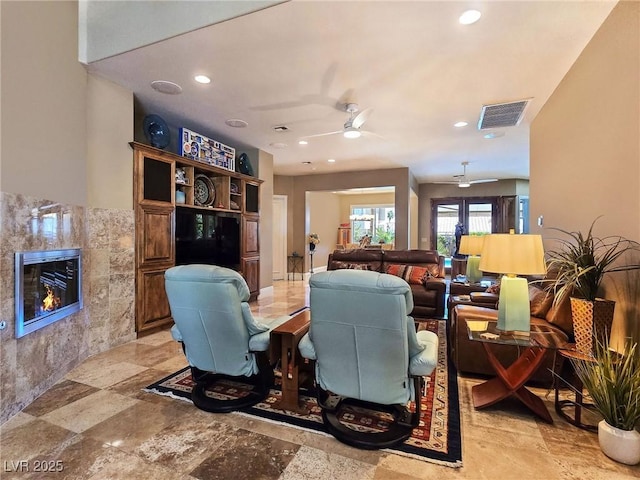 living area with a tiled fireplace, ceiling fan, and recessed lighting