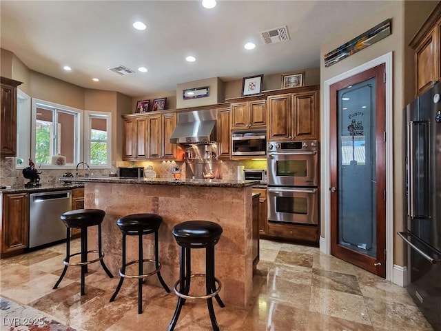 kitchen featuring stainless steel appliances, wall chimney exhaust hood, backsplash, a center island, and recessed lighting