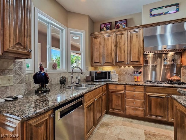 kitchen featuring stainless steel appliances, wall chimney exhaust hood, a sink, and brown cabinetry