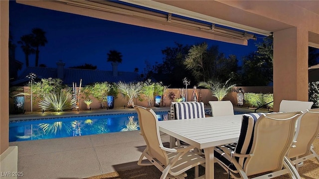 pool at night featuring a fenced backyard, a patio area, and outdoor dining space