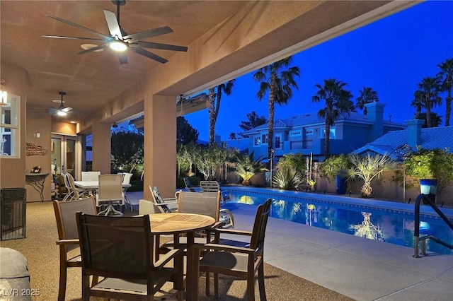 pool at night featuring ceiling fan, outdoor dining area, and a patio area