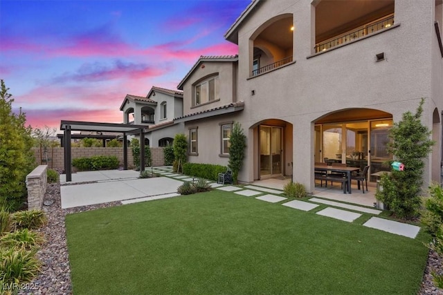 342 Molinetto St, Las Vegas, NV 89138 - back of property at dusk with stucco siding, a lawn, a patio area, fence, and a balcony