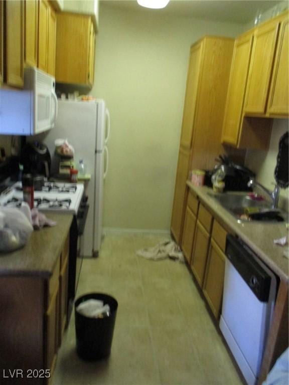 kitchen featuring white appliances, baseboards, and a sink