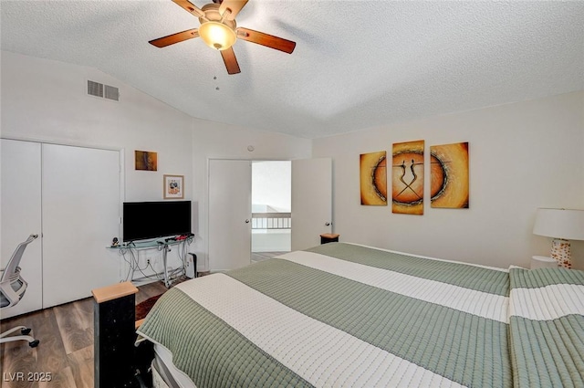 bedroom featuring a closet, vaulted ceiling, a textured ceiling, visible vents, and wood finished floors