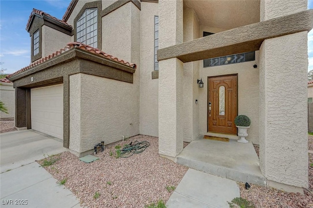 doorway to property with a tiled roof, concrete driveway, a garage, and stucco siding