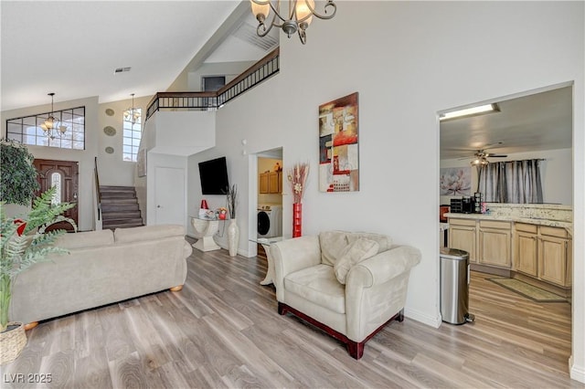 living room with stairway, light wood-style floors, washer / dryer, high vaulted ceiling, and ceiling fan with notable chandelier