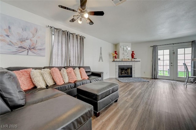 living room with a ceiling fan, visible vents, wood finished floors, a tiled fireplace, and baseboards