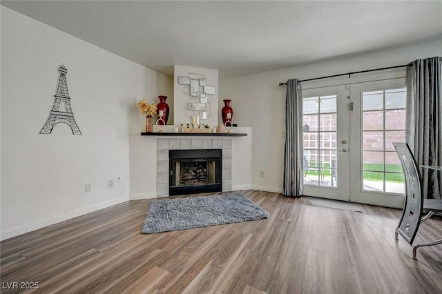 living area featuring a tile fireplace, french doors, baseboards, and wood finished floors