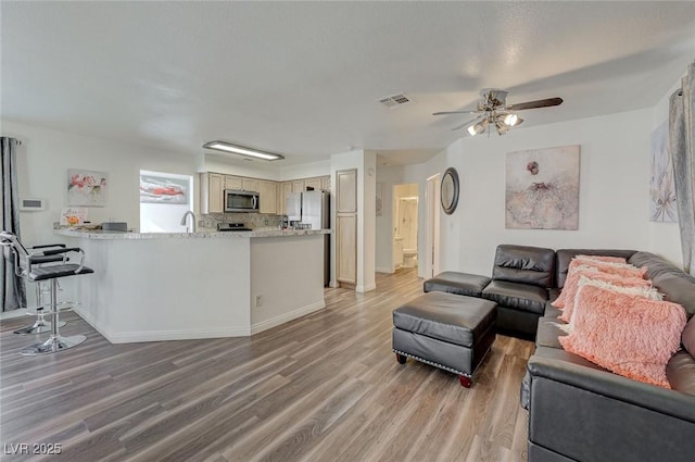 living room with light wood-type flooring, ceiling fan, baseboards, and visible vents