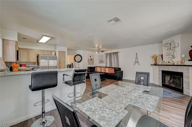 dining room with a fireplace, light wood-style flooring, a ceiling fan, visible vents, and baseboards