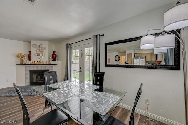 dining room with french doors, wood finished floors, baseboards, and a tile fireplace