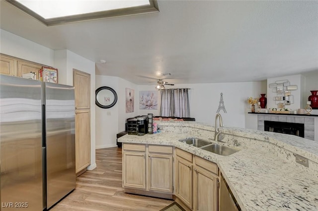 kitchen with light wood-type flooring, freestanding refrigerator, ceiling fan, a sink, and light brown cabinetry