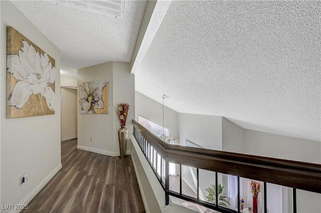 hallway with an upstairs landing, a textured ceiling, baseboards, and wood finished floors