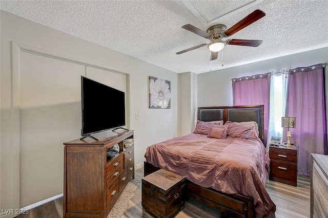 bedroom featuring light wood-style floors, a textured ceiling, baseboards, and ceiling fan