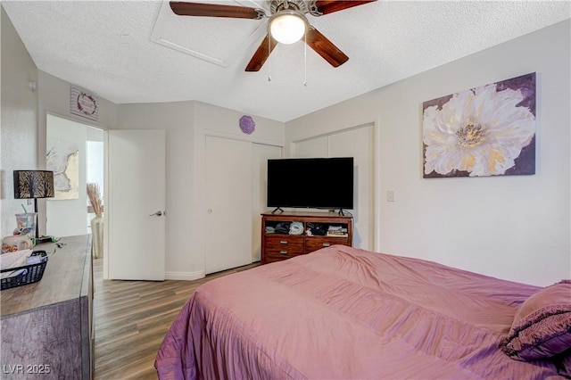 bedroom with a textured ceiling, a closet, a ceiling fan, wood finished floors, and attic access