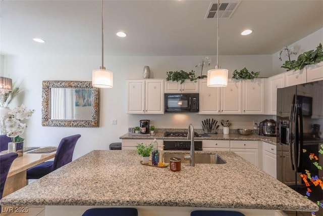 kitchen featuring light stone counters, white cabinetry, black appliances, visible vents, and a sink