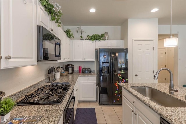 kitchen with light tile patterned floors, white cabinets, light stone countertops, black appliances, and a sink