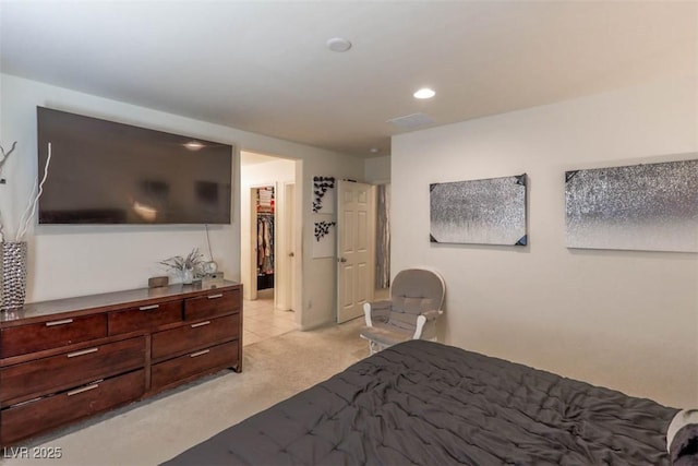 bedroom with recessed lighting, light colored carpet, and a walk in closet