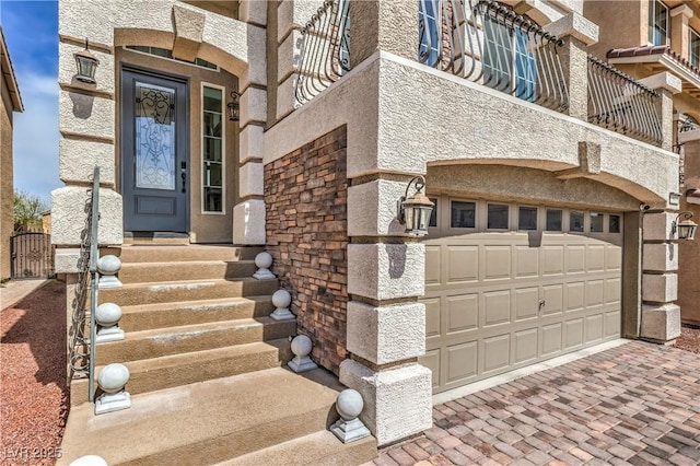 entrance to property featuring decorative driveway, stone siding, and a garage