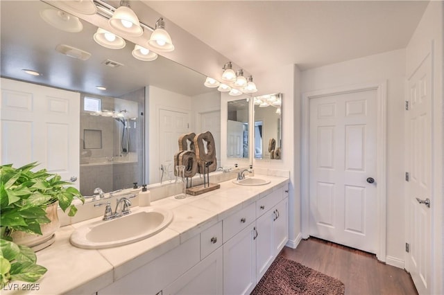full bathroom with a sink, visible vents, a shower stall, and wood finished floors