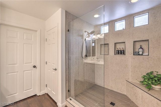 full bathroom featuring a sink, a tile shower, and wood finished floors