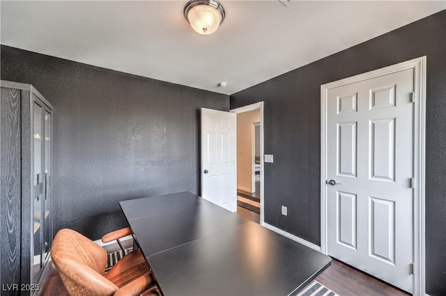 home office featuring dark wood-type flooring, a textured wall, and baseboards