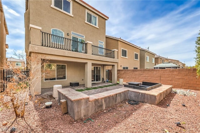 back of house featuring a patio area, a balcony, stucco siding, and fence