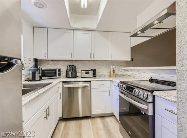 kitchen with stainless steel appliances, wall chimney range hood, white cabinets, and backsplash