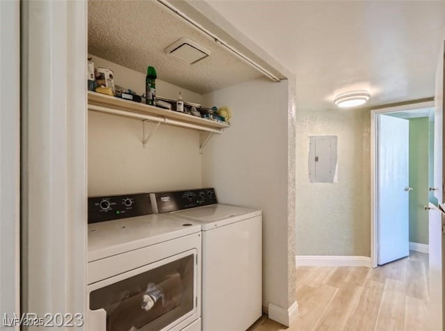 clothes washing area with washing machine and clothes dryer, electric panel, light wood-style floors, and baseboards