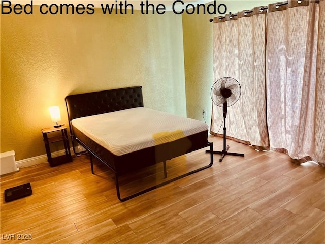 bedroom with wood finished floors, a textured wall, and baseboards